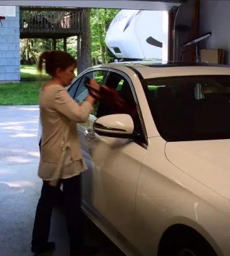 A woman is putting on her gloves while looking into the window of her car.